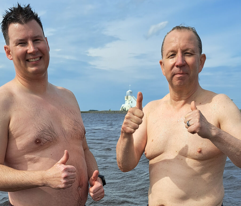 Kaksi miestä seisoo meressä peukalot pystyssä.