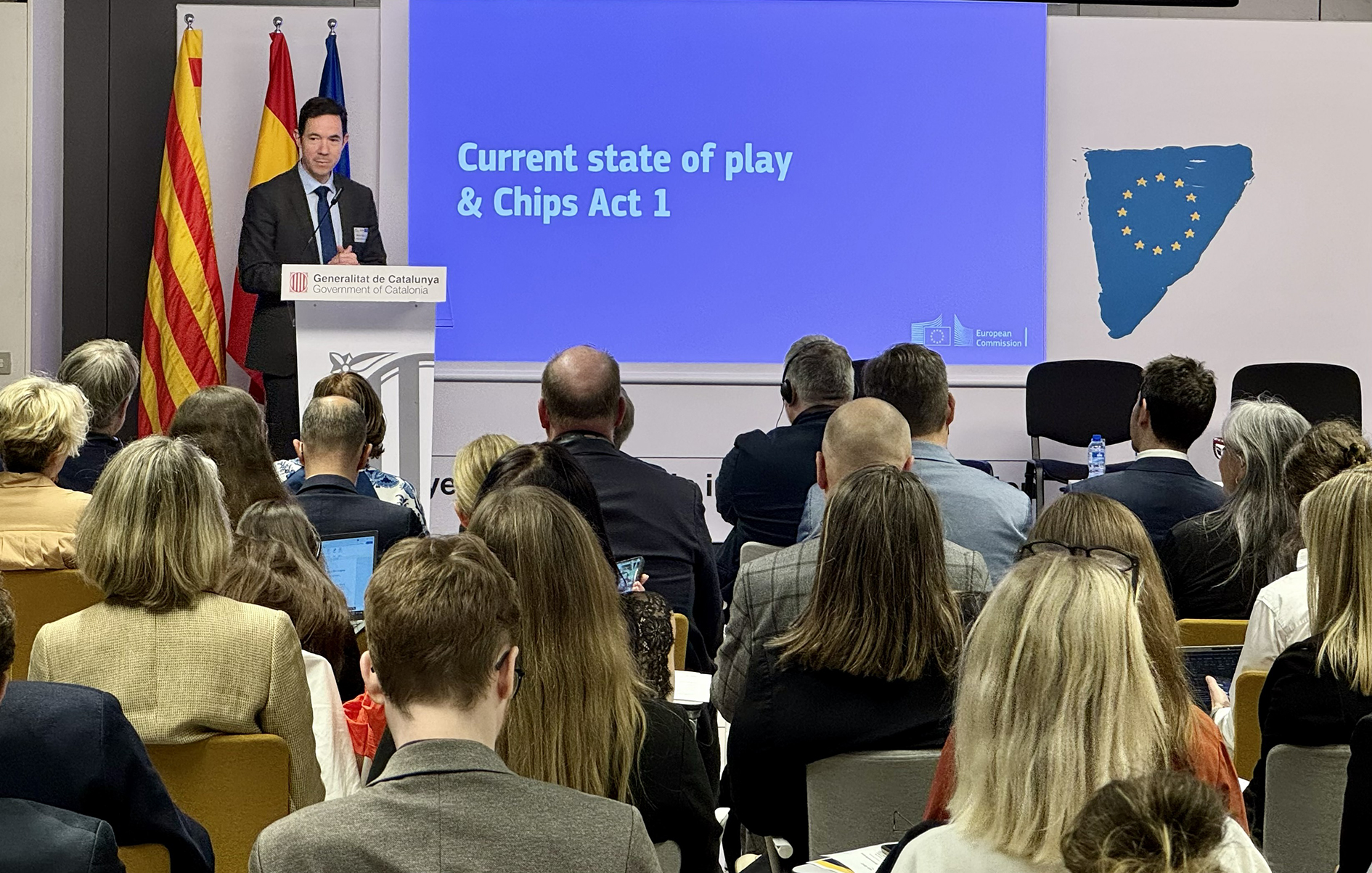 Espanjalainen, tummaan pukuun pukeutunut mies puhujakorokkeen takana taustallaan englanninkielinen teksti sinisellä pohjalla: "Current stat of play & Chips Act 1".